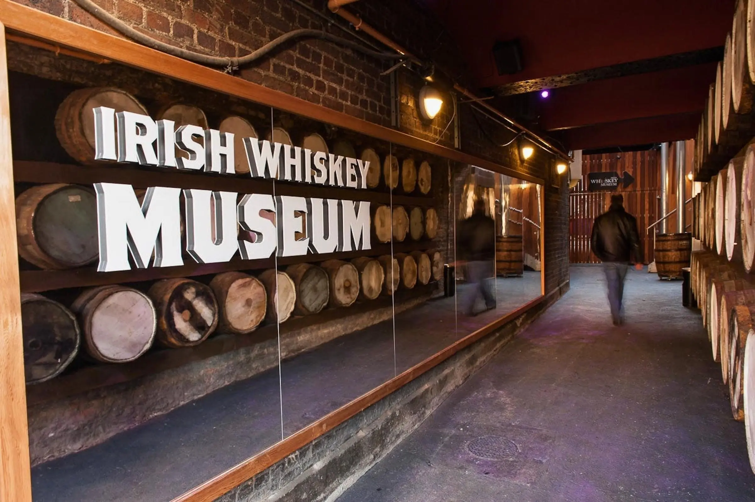 Large Irish Whiskey Museum sign over a glass display of wooden whiskey barrels in a brick corridor
