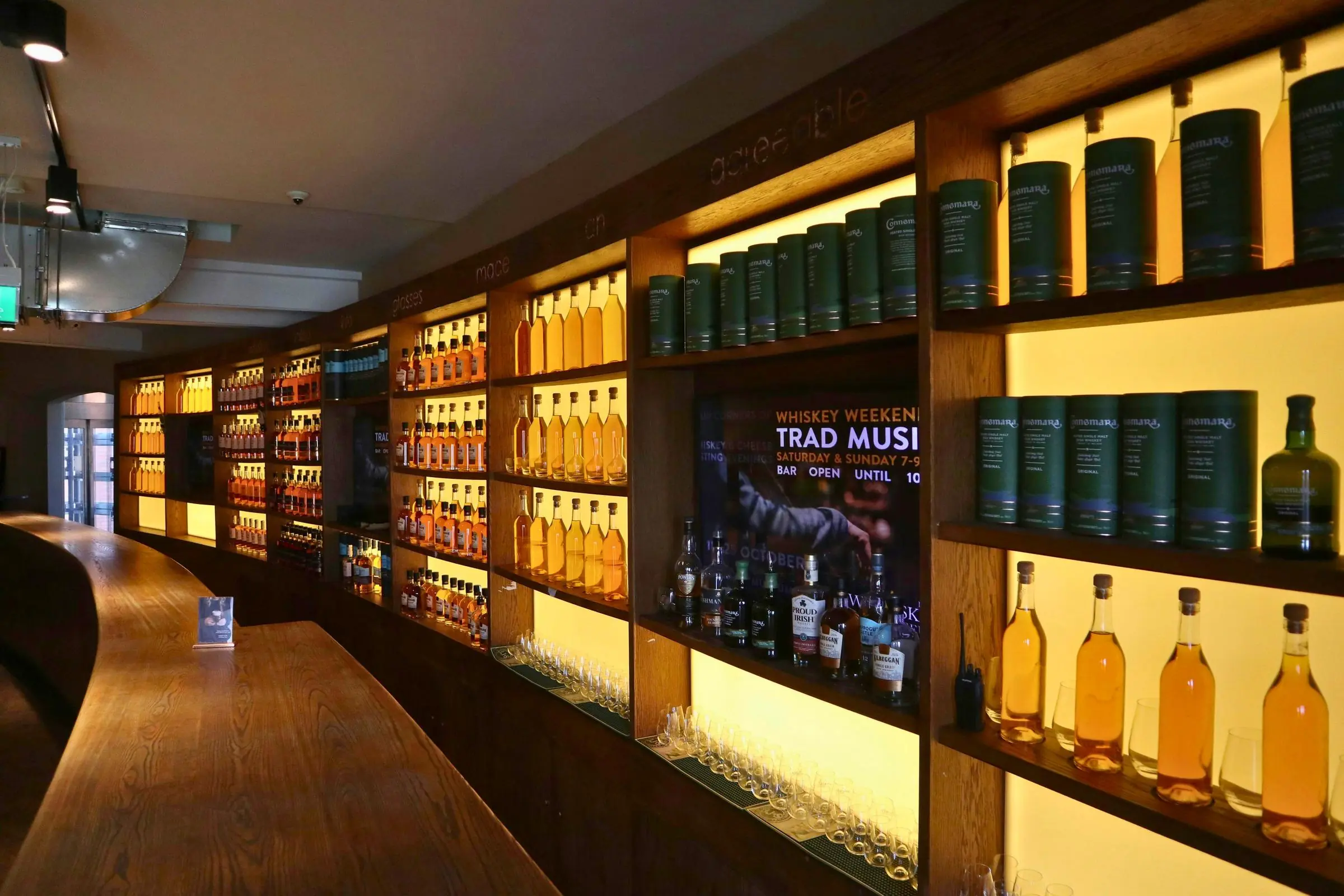 Curved wooden tasting bar and backlit shelves filled with whiskey bottles